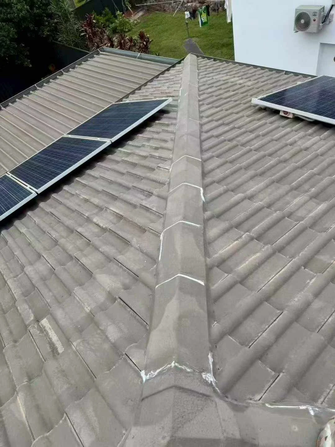 Ellis work photograph of ridge caps and grey roof tiles beside solar panels